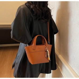 Detail einer braunen Leder-Beuteltasche mit Vintage-Perlenanhänger an einem Model