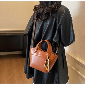 Detailansicht der braunen Leder-Beuteltasche mit Markenlogo und Perlen-Quastenanhänger