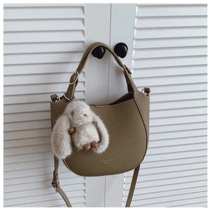 Gros plan du sac seau en cuir litchi kaki avec breloque lapin mignon sur une porte blanche