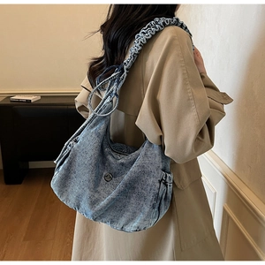 Close-up of vintage blue denim hobo bag featuring ruffled strap and metal logo detail