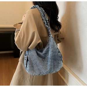 Detail of washed blue denim dumpling bag with pleated strap worn with a khaki trench coat