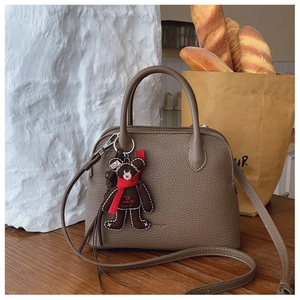 Detail of grey lychee leather handbag with cute bear charm and adjustable shoulder strap