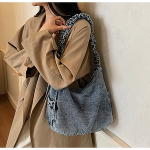 Detail of blue washed denim crescent bag featuring ruffled shoulder strap and metal logo