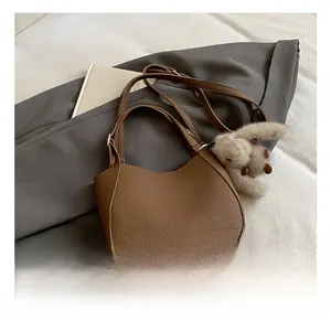 Brown litchi leather bucket bag featuring a plush rabbit charm and crossbody strap
