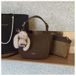 Détail d'un sac seau en cuir marron avec charm lapin en peluche et petite pochette