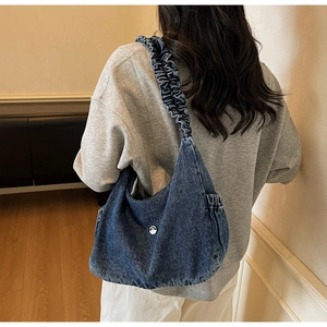 Detail of blue denim crescent bag with puffy cloud-style strap and metal logo buckle