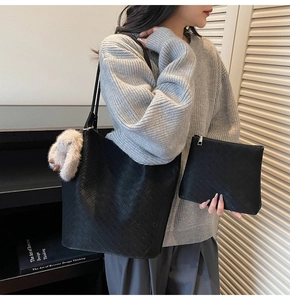 Detail view of a black woven tote bag with a white plush pompom charm and matching clutch