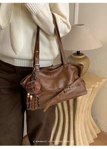 Close-up of retro brown PU leather shoulder bag with metallic eyelets and plaid cap charm