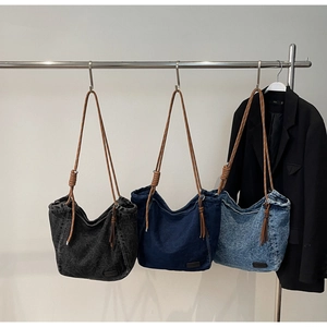 Three colors of denim tote bags with woven rope handles and tassels hanging on a rack