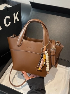 Braune Leder-Eimertasche mit Henkeln und Perlenanhänger auf einer Geschenkbox