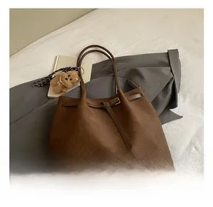 Dettaglio della borsa tote marrone intrecciata con manici sottili e ciondolo a orsetto