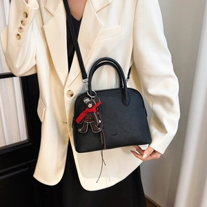 Detail of black lychee grain leather shell bag with cute bear charm and shoulder strap