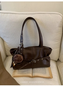 Detail view of coffee brown retro tote bag with unique plaid beret charm on soft white fabric