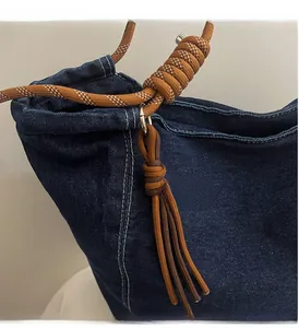 Detail of denim tote bag with thick woven rope handle and tassel charm