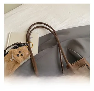 Dettaglio della texture in pelle intrecciata marrone con ciondolo a orsetto e fibbie d'oro