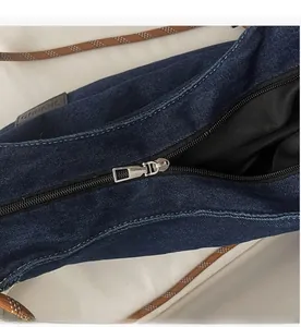 Detail of silver metal zipper and brand leather tag on blue denim tote bag