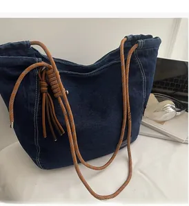 Detail of blue denim tote bag with brown rope handle and tassel on office desk