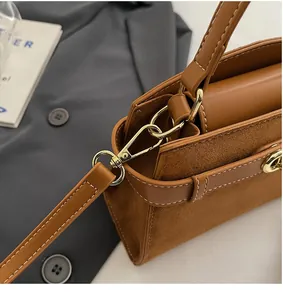 Detailaufnahme von goldenem Verschluss und Nähten der braunen Handtasche
