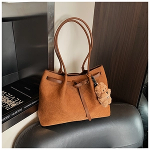 Dettaglio della borsa tote intrecciata color caramello con ciondolo a orsetto e nodo