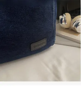 Detailed close-up of dark blue denim tote fabric with white stitching and leather brand tag