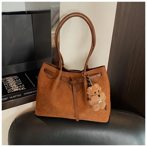 Dettaglio della borsa tote in pelle scamosciata marrone con trama intrecciata e orsetto
