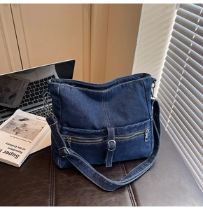 Close-up of dark blue denim tote bag texture and front zipper pocket detail with metal buckle