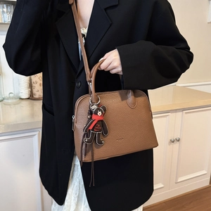 Close-up of brown lychee grain leather shell bag with cute plush bear charm detail