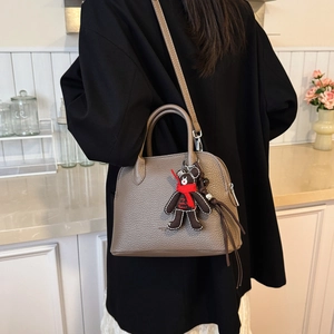 Detail of grey lychee leather handbag with cute bear charm and adjustable shoulder strap