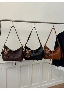 Trois grands sacs à bandoulière en marron foncé, noir et caramel sur un support en métal