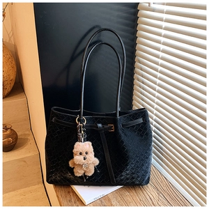 Dettaglio della borsa tote in pelle nera intrecciata con ciondolo a forma di orsetto