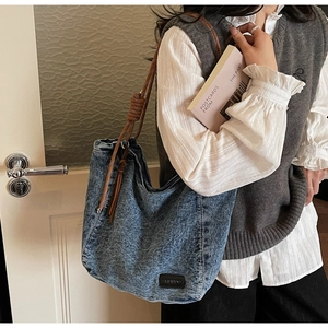 Detail of vintage denim tote bag with brown woven rope strap and branded leather patch