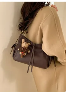 Détail du sac à bandoulière en cuir marron foncé avec cordon de serrage et breloque en peluche