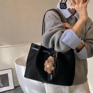 Dettaglio borsa tote intrecciata nera con ciondolo a forma di orsetto e sciarpa di seta stampata