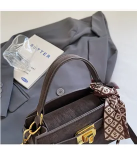 Detail of dark brown handbag with gold hardware, silk scarf handle, and matte texture finish