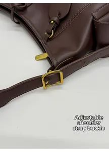 Détail macro de la bandoulière réglable avec boucle dorée sur un sac en cuir marron