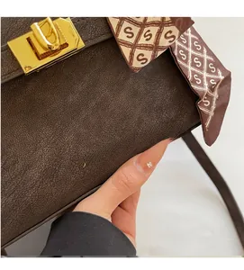 Close-up of brown textured leather bag with gold hardware and decorative silk scarf