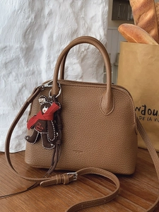 Brown lychee leather shell handbag with bear charm on wooden table in French style