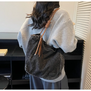 Détail d'un grand sac fourre-tout en jean noir avec anses tressées brunes et pompons
