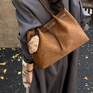 Dettaglio ravvicinato della borsa tote marrone intrecciata con piccolo orsetto peluche