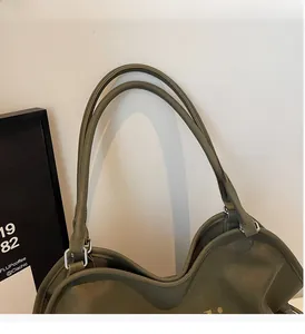 Detail of dark olive green leather tote bag featuring reinforced handles and silver buckles