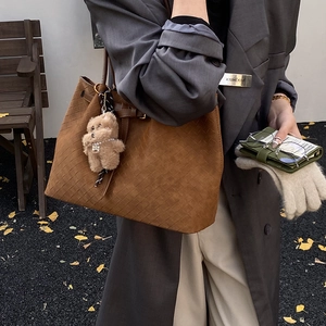 Dettaglio della trama intrecciata della borsa tote in pelle marrone con ciondolo a orsetto