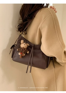 Détail d'un sac bandoulière en cuir marron foncé avec lanières et un charmant ours en peluche