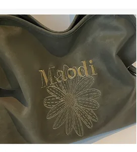 Close-up of floral daisy embroidery and Maodi logo on dark green vintage leather tote bag