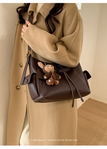 Détail du sac bandoulière en cuir mat marron foncé avec un charmant ours au crochet