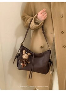 Détail du sac à bandoulière rétro en cuir marron foncé avec charme d'ours sur manteau