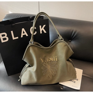 Close-up of olive green tote bag with daisy embroidery on a black leather sofa