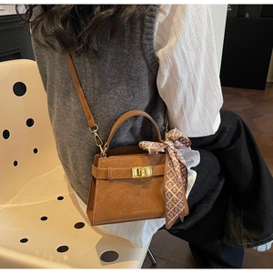 Detail of brown suede handbag featuring a gold lock and decorative printed silk scarf