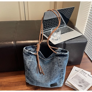 Detail of blue washed denim tote bag with thick brown woven rope straps and knot detail