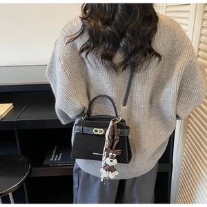Detail einer schwarzen matten Leder-Handtasche mit Karoschal und Hundeanhänger am Model