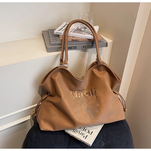Detail view of brown faux leather tote bag featuring daisy embroidery and thin handles